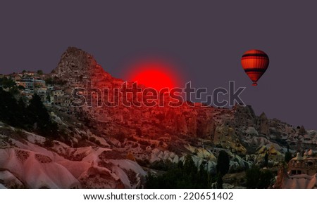 Hot air balloon flying over Cappadocia with dark red sun