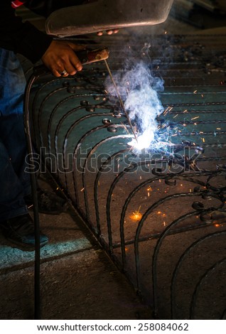Blacksmith working on wrought iron using welding equipment making beautiful blue light from torch