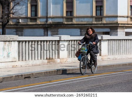 VERONA, ITALY - MARCH 23, 2015: Senior woman riding bike with market bag on a bridge