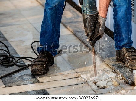Builder worker with pneumatic hammer drill perforator equipment making hole in marble at construction site