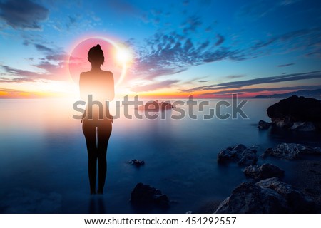 Silhouette of a slim girl standing on a beach watching solar eclipse