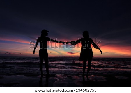 young couple in love hold hands together, with background of sunset evening glow on Karon beach, Phuket, Thailand.