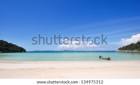 Clean and pure view of tropical white sand beach and ocean and blue sky, with single boat floats ashore. Shot  on Raya Island, Phuket, Thailand.