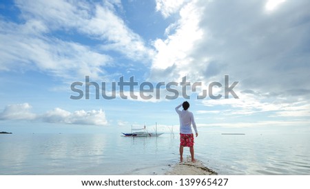 Back portrait of single young man stands on tip of the beach and looks to the horizon. Shot on Virgin Island, Panglao, Bohol, Philippines, known to many locals as the Ã¢Â?Â?hidden oasisÃ¢Â?Â�.