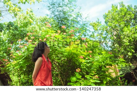 Back portrait of single young girl looking at the blossoming flowers and trees. Shot in Bee Farm, Panglao, Bohol, Philippines.