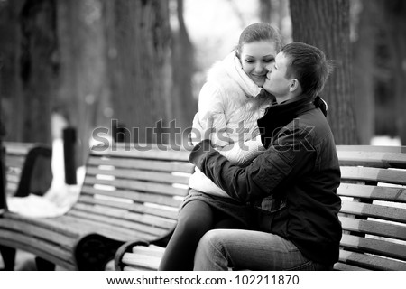 Black and white portrait of young couple sitting on bench in park and hugging