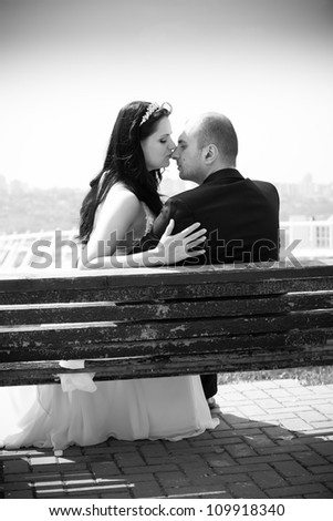 Black and white photo of newly married couple kissing on bench in park