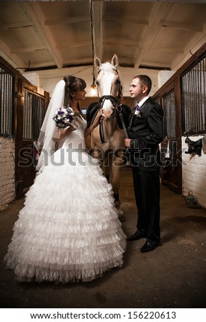 Newly married couple posing in stable with horse