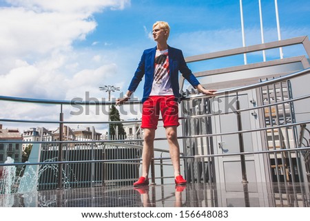fashionable man in red shorts posing near railings