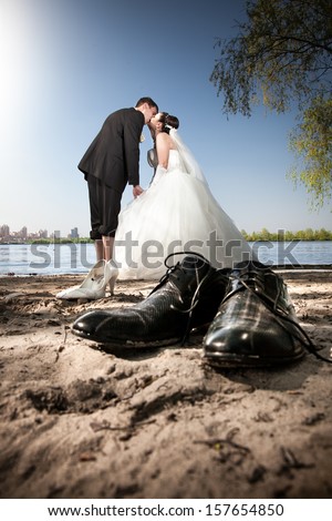 Married couple kissing on beach. Grooms shoes standing in front of them