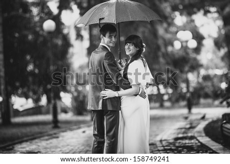 Black and white portrait of married couple standing in park under umbrella