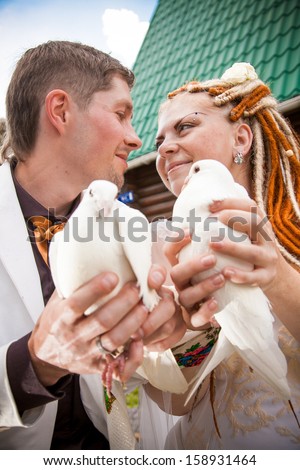 Bride and groom looking at each other and holding two pigeons close to each other
