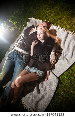 Beautiful couple in love lying on plaid on lawn at night