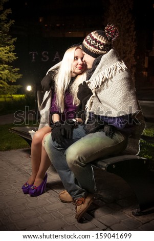 Beautiful couple sitting on bench in autumn park at night