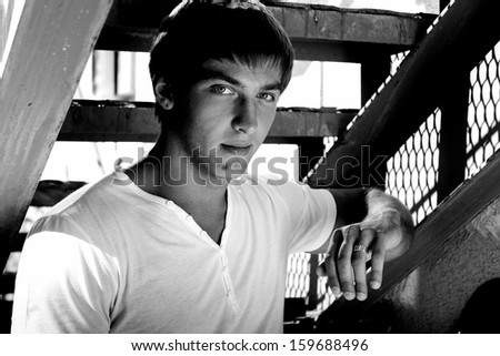 Black and white portrait of muscular man standing under metal staircase