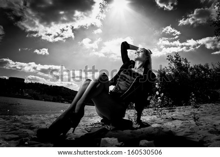 Black and white portrait of sexy blonde girl sitting on beach against sun