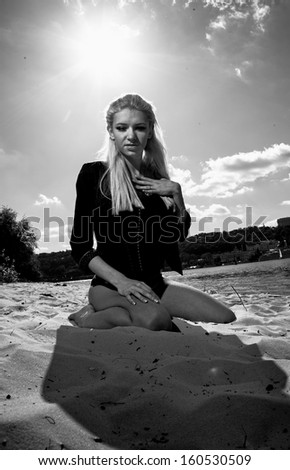 Black and white portrait of sexy girl in black coat sitting on knees on beach