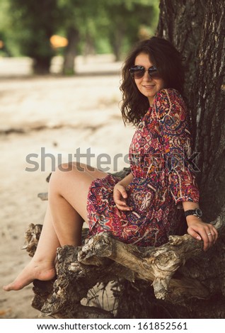 Toned full length portrait of romantic girl in dress sitting under tree