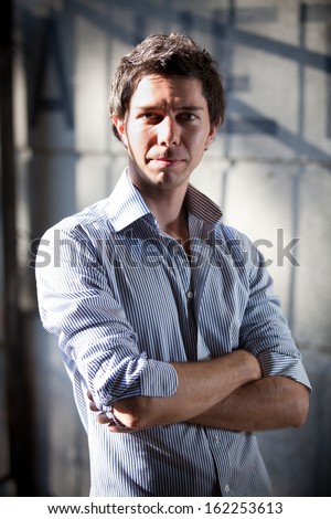 Handsome stylish man in blue shirt posing on street with crossed arms