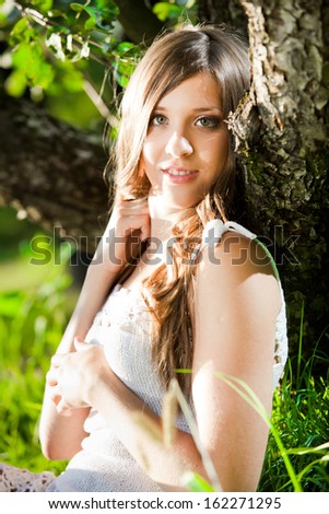 Closeup portrait of brunette girl leaning to tree and smiling in sun rays