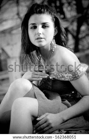 Black and white portrait of sad woman in dress sitting outdoor