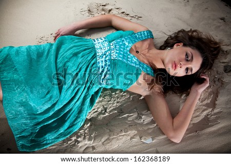 Beautiful woman in blue dress lying on sand dune
