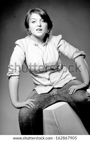 Black and white portrait of woman with big breast in shirt and jeans sitting on white cube