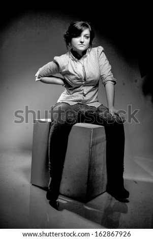 Black and white portrait of sexy woman in jeans sitting on white cube