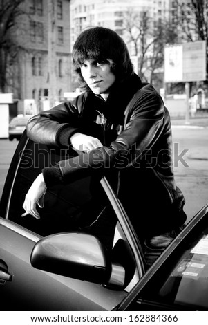 Black and white portrait of fashionable man leaning to car door and smoking cigarette