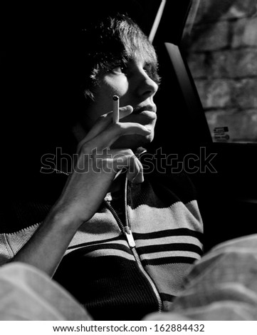 Black and white portrait of handsome man smoking cigarette in car cabin and looking out of window