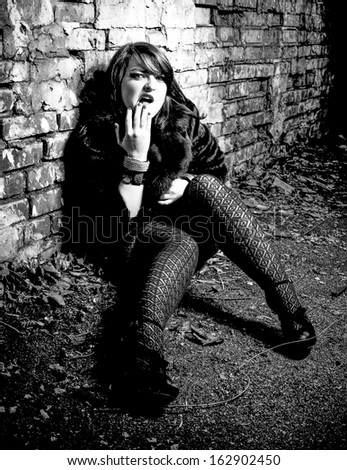 Black and white portrait of sexy woman sitting near wall and crying