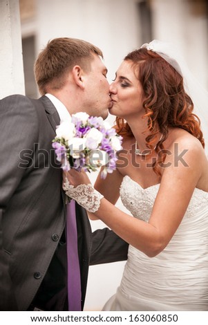 Closeup portrait of bride kissing handsome groom while holding wedding bouquet