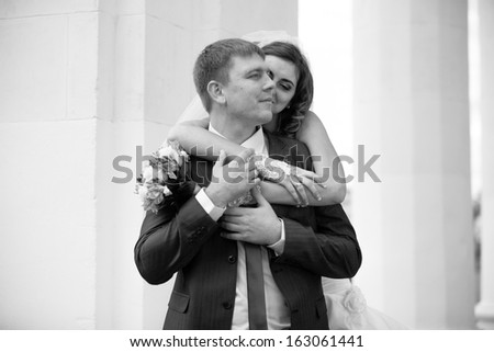 Black and white portrait of bride hugging groom from back and whispering on his ear