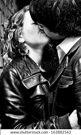 Black and white closeup portrait of young couple kissing passionately while leaning against wall