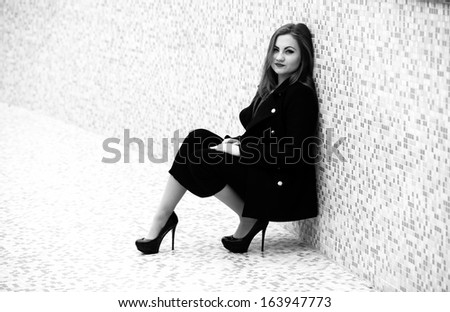 Black and white portrait of sexy woman sitting in black dress and leaning against tiled wall