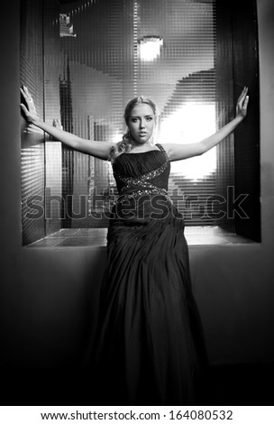 Black and white portrait of woman in black dress sitting against big mirror on wall