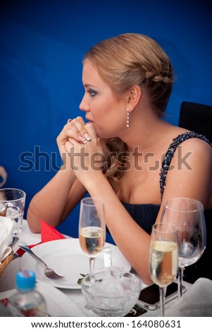 Sexy elegant woman sitting at table in restaurant against blue wall