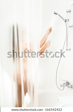 Beautiful brunette woman washing in shower behind transparent curtain