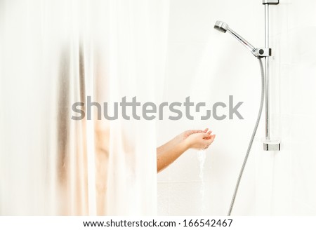 Sexy woman standing behind curtain at shower and holding hands under water stream