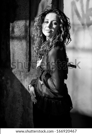 Black and white portrait of sexy curly woman in blouse posing against wall on street