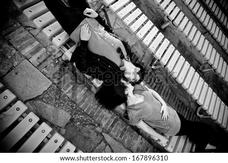 Black and white portrait of couple lying face to face on bench and kissing