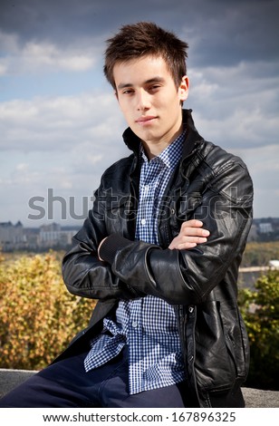 Closeup portrait of handsome guy in black coat posing against beautiful landscape