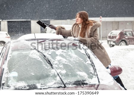 Portrait of young woman cleaning snow from car roof using brush