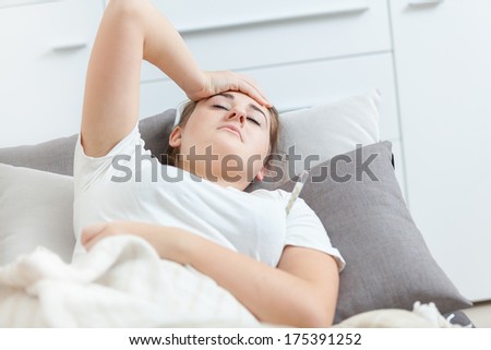 Closeup portrait of sick woman lying in bed and holding hand on head