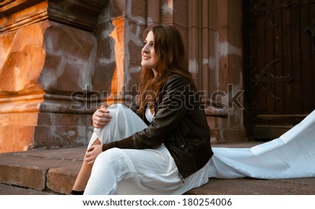 Beautiful brunette girl dreaming on stairs of old castle at sunset