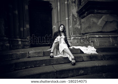Black and white photo of woman in long dress sitting on stone stairs at castle