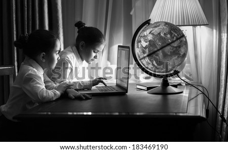 Black and white portrait of two girls typing e-mail on laptop at night