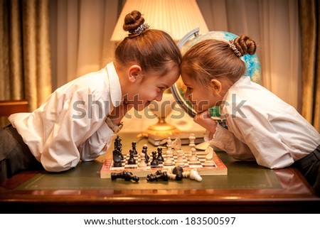 Two little sister playing chess and looking eye to eye