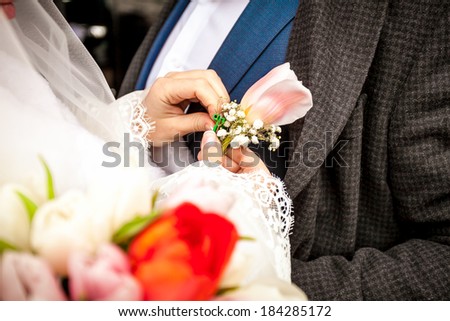 Closeup photo of bride adjusting boutonniere on grooms jacket