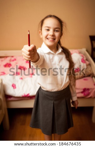 Blurred portrait of smiling schoolgirl holding red pencil
